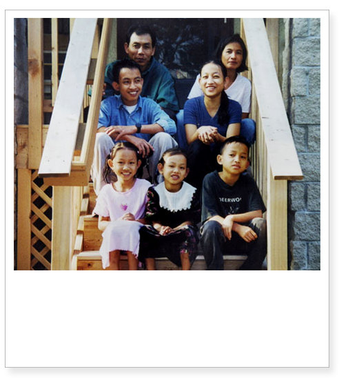 A family with two adults and five children sit on the front entry steps of a home.