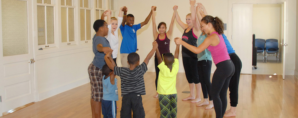 Photograph of 11 university students and local youth standing in a circle and holding their hands in the air.