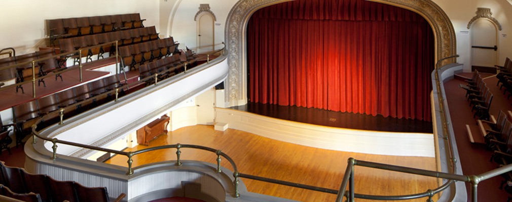 Photograph taken from the balcony showing the proscenium stage and wood floor of the auditorium.