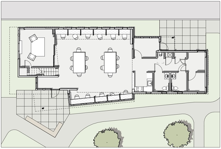 Floor plan of the community center showing the building entrance, a partially enclosed room and the stairway to the loft on the left side of the building. The center portion of the building is one large area accommodating 10 desk carrels along the outside walls and two 6-seated tables in the middle of the room. The right side of the building contains ancillary rooms, including a staff office, a small kitchen, and restrooms.