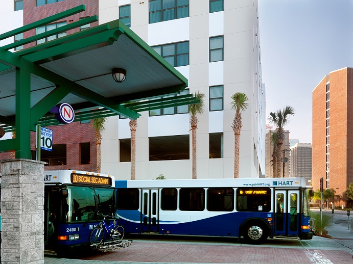 A photograph taken at street level of two buses in the Marion Transit Center, with the Metro 510 apartment building in the background.