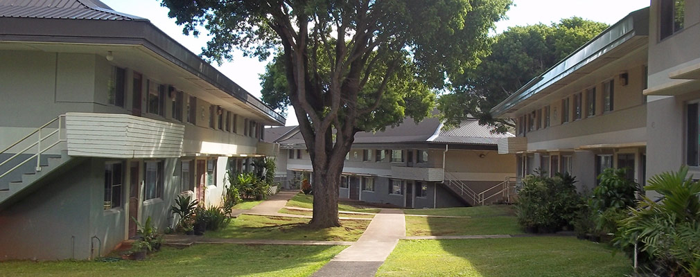 Photograph of three two-story residential buildings with a connecting lawn and concrete walkway. 