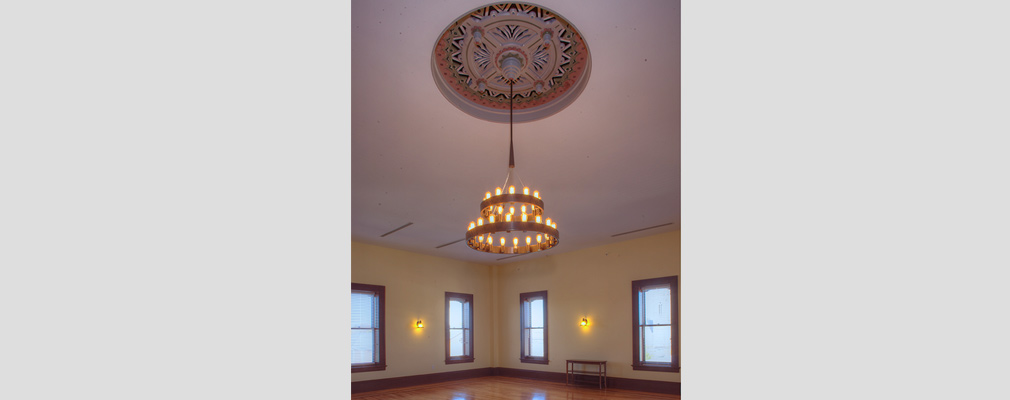 Photograph of a two-tiered chandelier descending from a ceiling medallion in a large room. 