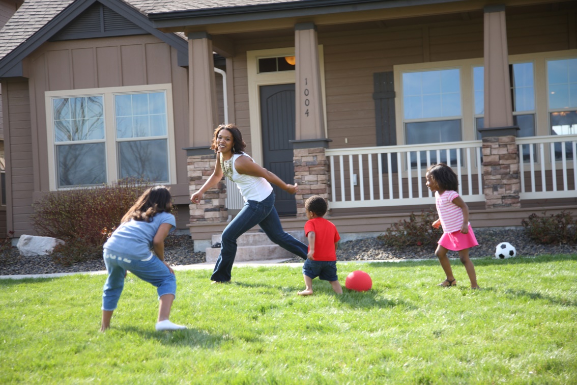 A woman is playing with three children in the front yard of a house.