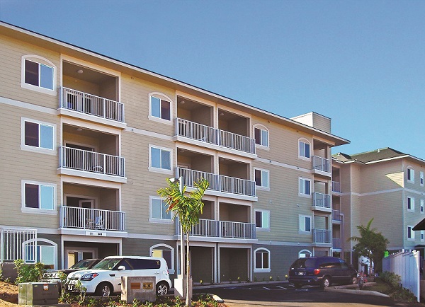 Photograph of the front façade of a four-story multifamily building with vinyl siding.