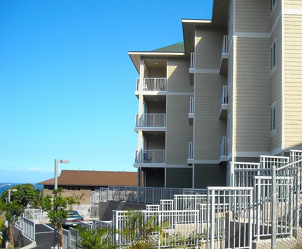 Photograph of the side of the four-story building with several balconies; Kahului Bay is in the background. 
