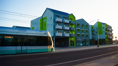 Photograph showing a light-rail car about to pass in front of a four-story building.