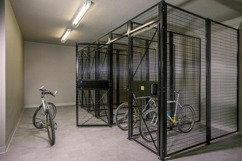 Photograph of six wire bicycle cages in a room, with two bicycles inside and one bicycle parked outside the set of cages.