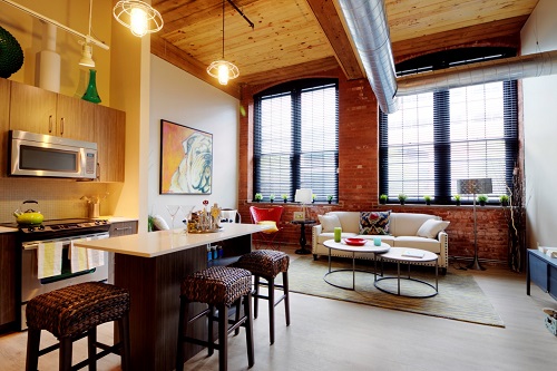 Photograph of the kitchen and living area in a Winchester Lofts unit with a very high ceiling and four large windows. 
