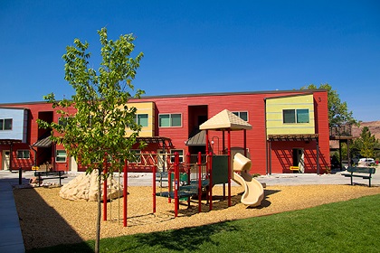 Picture taken at ground level showing playground equipment in front of a two-story residential building.