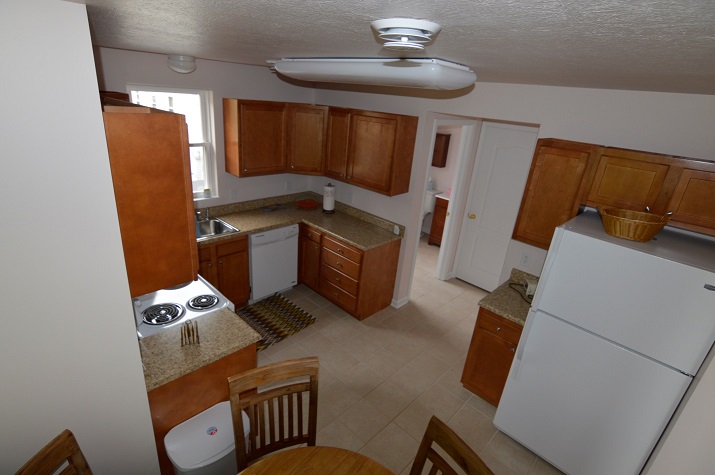 Photograph a kitchen showing a refrigerator, electric stove, and dishwasher, as well as an eating area.