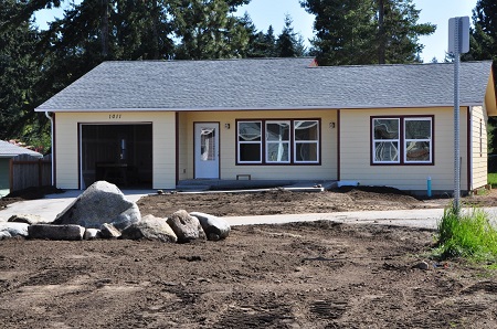 Photograph of the front façade of a one-story, single-family home as construction nears completion. The house includes an attached garage.