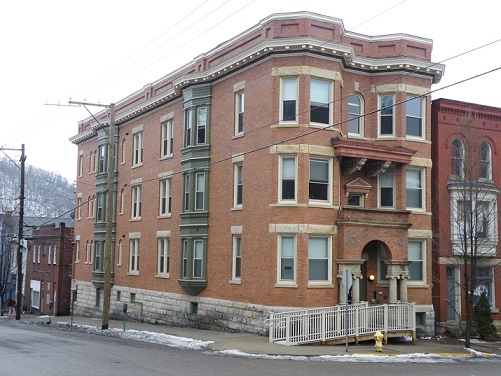 Photograph of a three-story brick building at the intersection of two streets. A ramp leads to the main entrance.