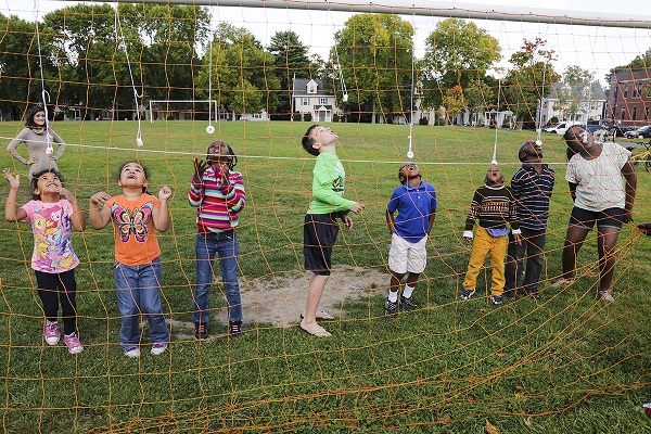 Photograph of eight children  biting at donuts hanging on strings from a soccer goal as an adult supervises in the background.