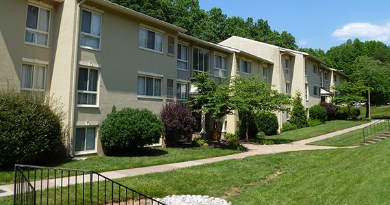 Exterior image of three-story multifamily buildings, connected by sidewalks and flanked by trees and shrubs.