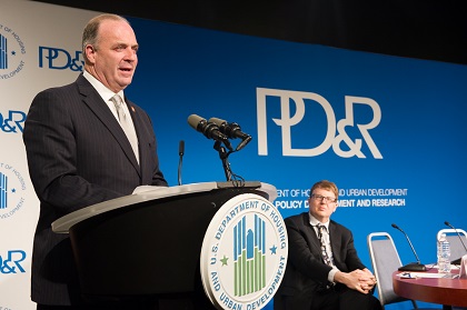 U.S. Congressman Dan Kildee stands behind a podium bearing the HUD logo, addressing attendees (not pictured). Todd M. Richardson, Associate Deputy Assistant Secretary at PD&R, is visible in the background, seated in front of a PD&R banner.