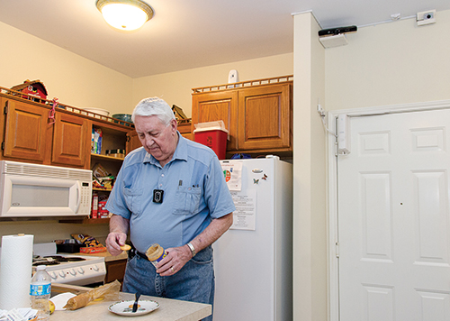 An 85-year-old man making a snack in his kitchen where an electronic sensor on the wall can call for help if he experiences a fall.