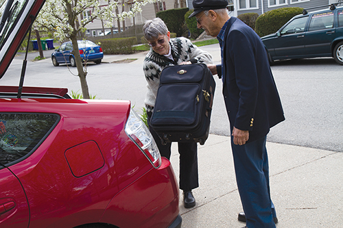 A Newton at Home volunteer driver loading an elderly man’s suitcase in the trunk of her car in preparation for providing him with a ride.