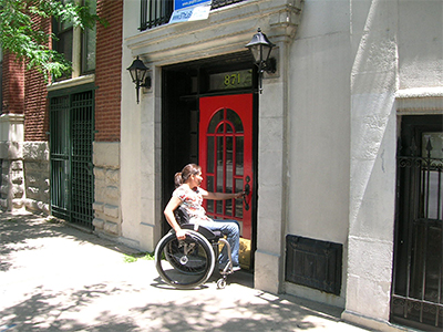 Woman in wheelchair opening the door to a multifamily building.