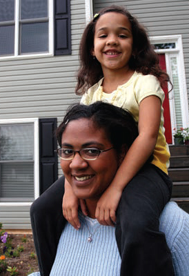 A mother and daughter pose in front of a home.