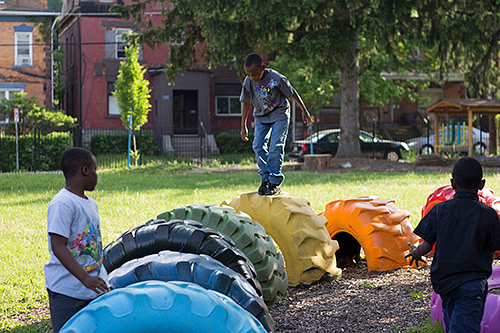 A greened and repurposed vacant lot, converted to a play area in which children are shown playing.  