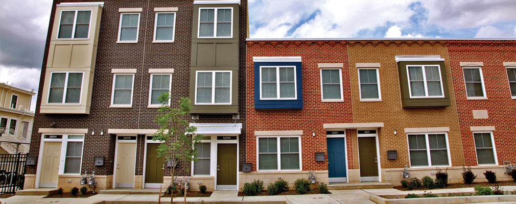 Multi-colored two- and three-story walkup apartment buildings with sidewalk in foreground.
