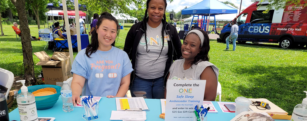Photograph of three women at a CelebrateOne informational table at an outdoor event.
