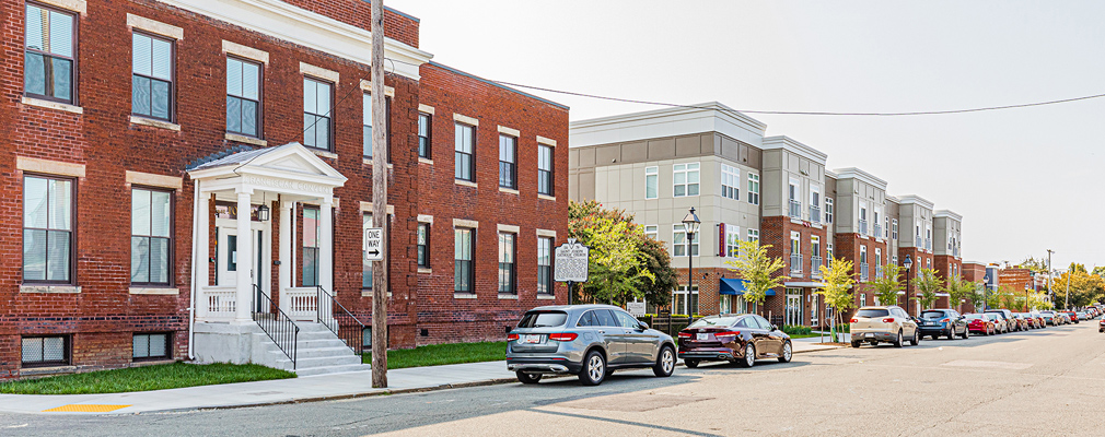 Photograph of a historic, two-story brick building next to a newly constructed, three-story residential building. 