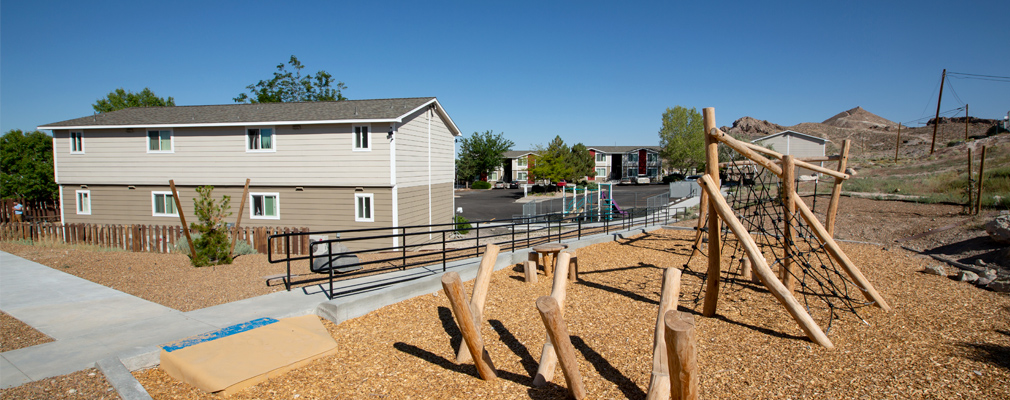 Wooden play structures beside a walkway, with a two-story residential building in the middle ground.