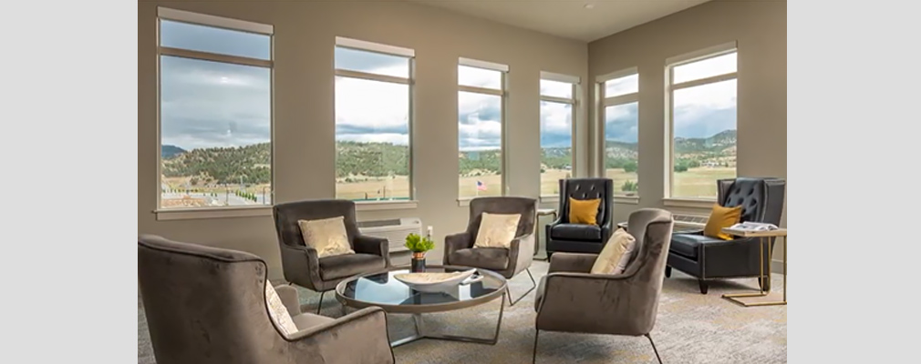 An interior room with various armchairs, a coffee table, and six windows overlooking a mountain range.
