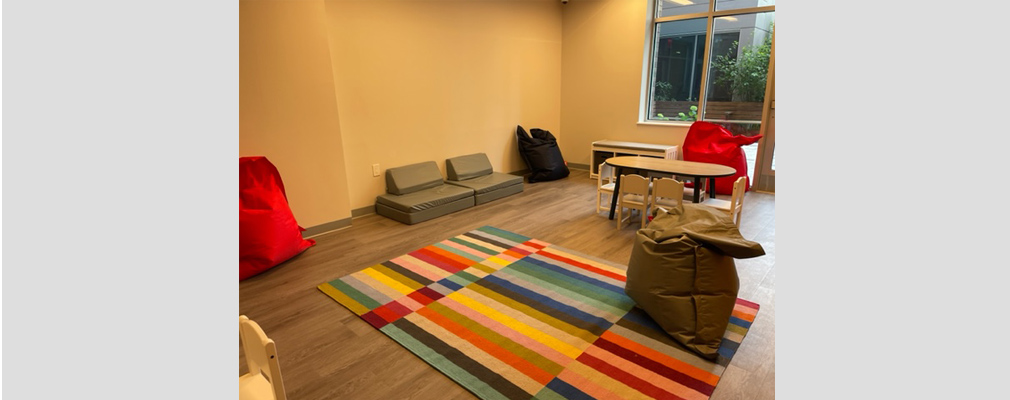Image of a childcare room with furniture and a colorful rug.
