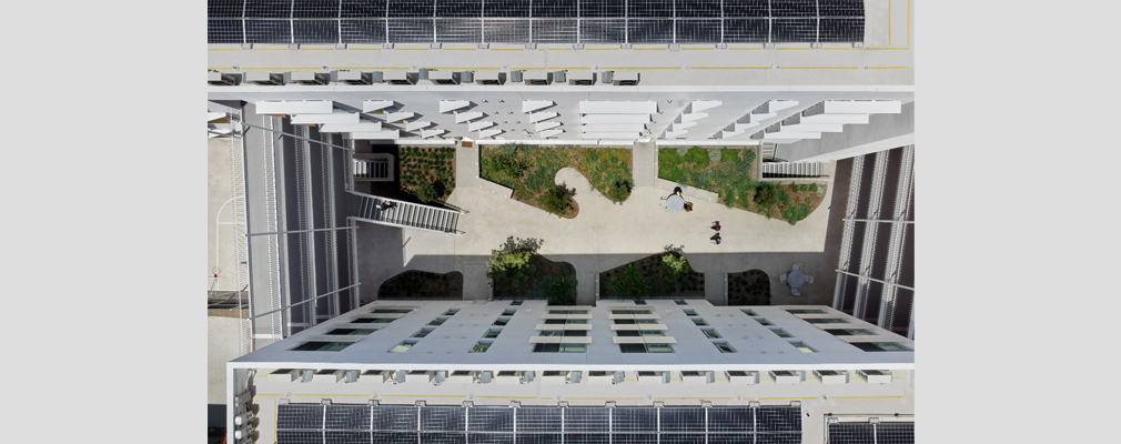 Aerial photograph of a landscaped courtyard framed by two wings of a five-story residential building and two sets of connecting walkways, with solar panels on the roofs of the two wings.