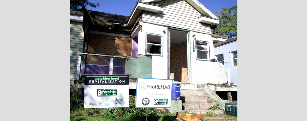 Photograph of a single-story house during renovation, with two signs in the foreground identifying project partners 8twelve Coalition and ecoREHAB.