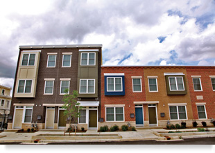 Multi-colored two- and three-story walkup apartment buildings with sidewalk in foreground.