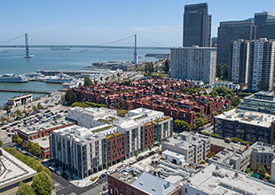 An aerial photograph of an urban development with low-rise buildings in the foreground and skyscrapers, San Francisco Bay, and a bridge in the background.
