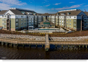 A pool in between two 4-story apartment buildings that face the river and boardwalk.