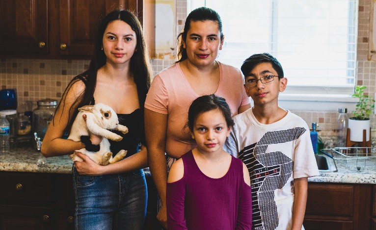 A family of four with one of them holding a rabbit and standing in front of a kitchen counter.