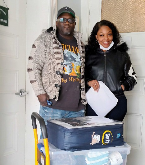 A man and a woman standing with a mattress bag and plastic storage box in front of them.