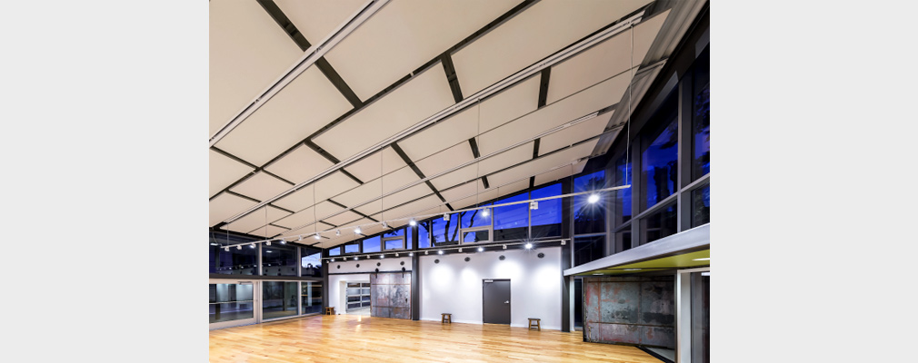 Photograph of interior of a large two-story performance space with a wooden floor and a slanted ceiling covered in specially crafted pads.