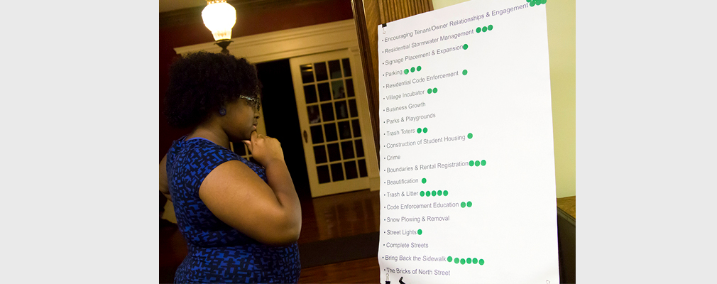 A woman looks at a poster-sized list of projects that residents have used to indicate their preferred neighborhood improvement projects.