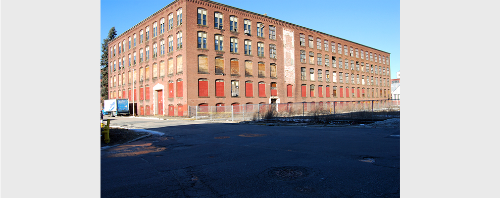 Photograph of two façades of a five-story brick industrial building prior to renovation.