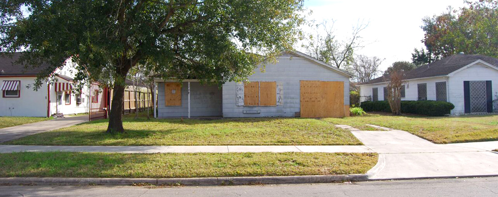 Photograph of the front façade of a boarded-up single-family house damaged by Hurricane Ike.