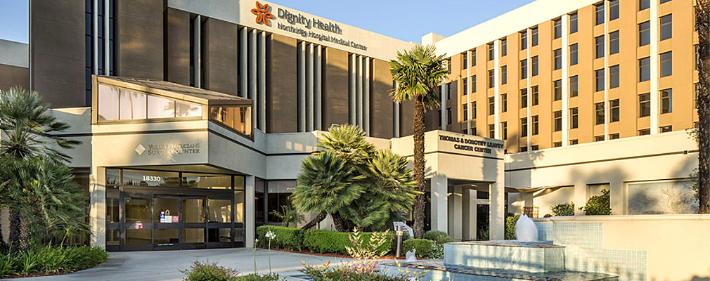 Photograph of the front façade of a six-story institutional building with a sign that reads “Dignity Health Northridge Hospital Medical Center.”
