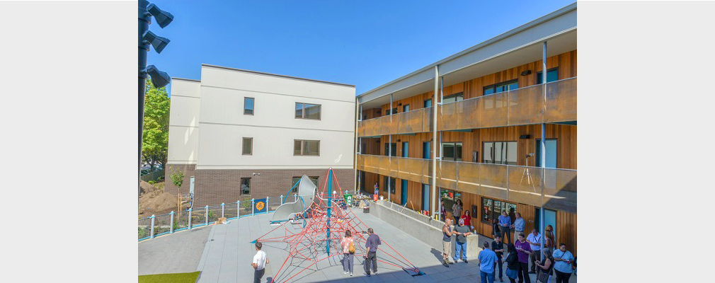Photograph of adults and children in a playground occupying the courtyard of a three-story apartment building.
