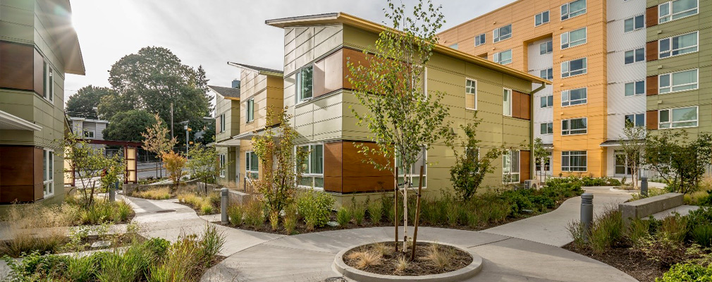 Photograph of three 2-story townhouses in front of a 6-story apartment building, with a courtyard in the foreground.