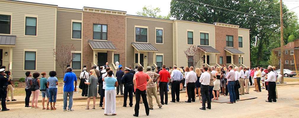 Photograph of a crowd of community members standing in front of five new two-story townhouses.
