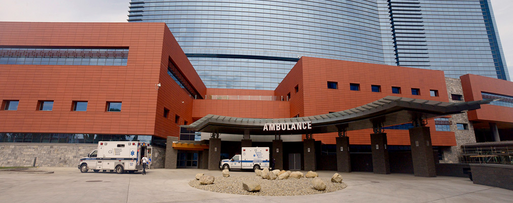 Photograph of the glass and red brick front façade of Stamford Hospital, with two ambulances parked in front. 