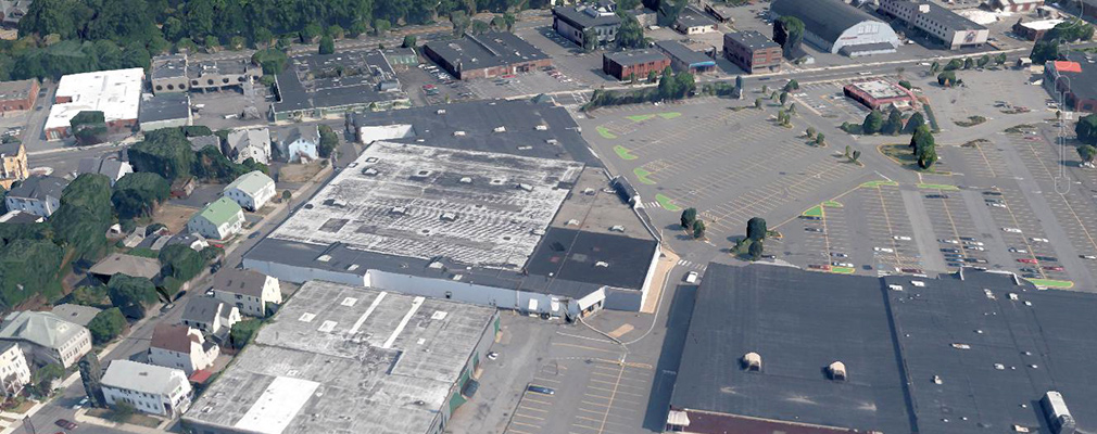 Low-angle aerial photograph of a shopping center on a large block bordered by commercial developments and residences.
