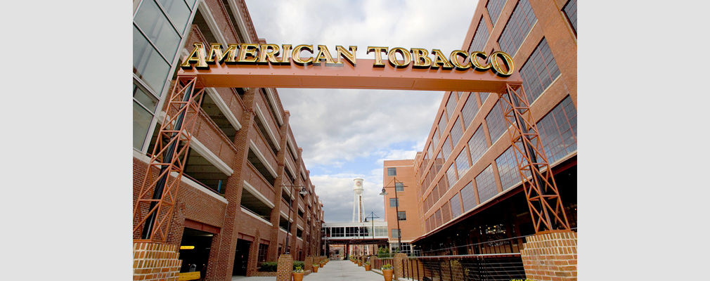 Photograph of a walkway between two 5-story buildings with a sign over the walkway reading, “American Tobacco.”