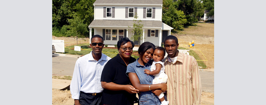 Photograph of four adults and an infant in front of a newly constructed two-story single-family detached house.